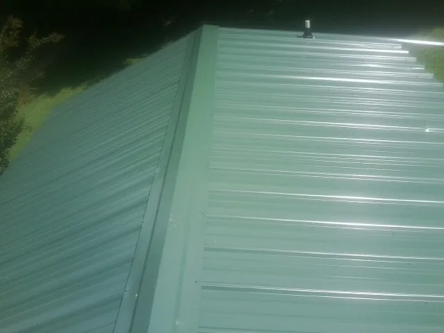 New green metal panels meeting at the ridge of a roof — Flat Roof Repair work by our crew in Stanton